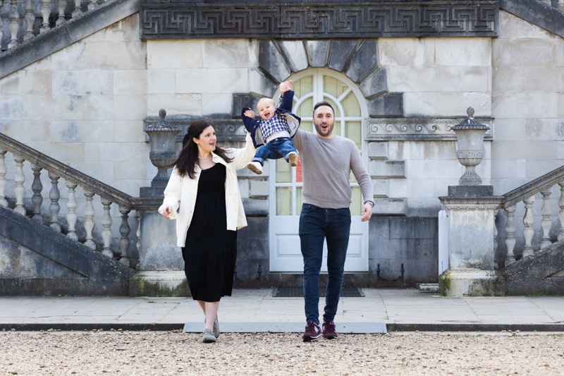 man and lady swinging a little boy in front of a beautiful building