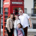 Man, lady and two girls in front of a red London telephone box