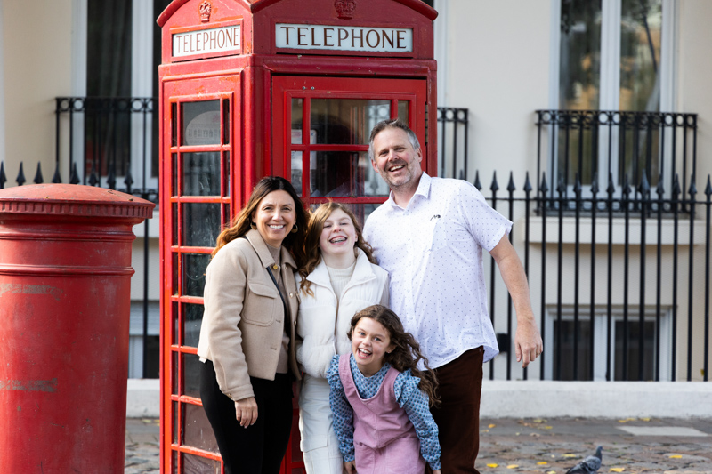 Man, lady and two girls in front of a red London telephone box