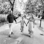 Man, boy and lady walking through a park holding hands.