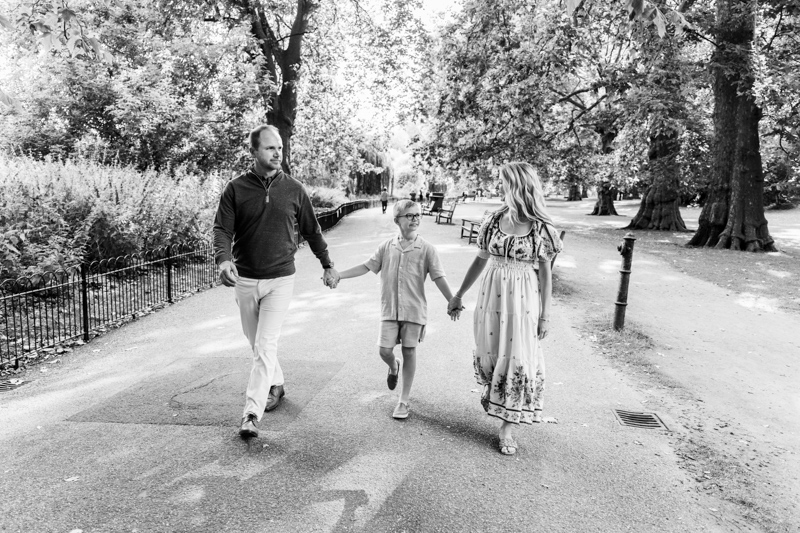 Man, boy and lady walking through a park holding hands.