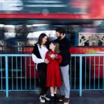 man, lady and girl in front of blurred red London bus