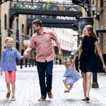 Family of four walking down a cobbled street, the girl being swung by her parents.