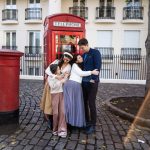 man, lady and two girls hugging in front of red telephone box and red letter box