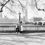 mum and dad kissing and holding their baby in front of the houses of parliament