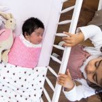 little girl looking at baby in cot